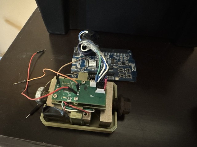 Open rower telemetry prototype: the PCB mounted inside the 3D-printed enclosure, a wireless module with a coiled loop antenna, the rotary knob and cam lever, and jumper wiring, with a second board on the desk behind.
